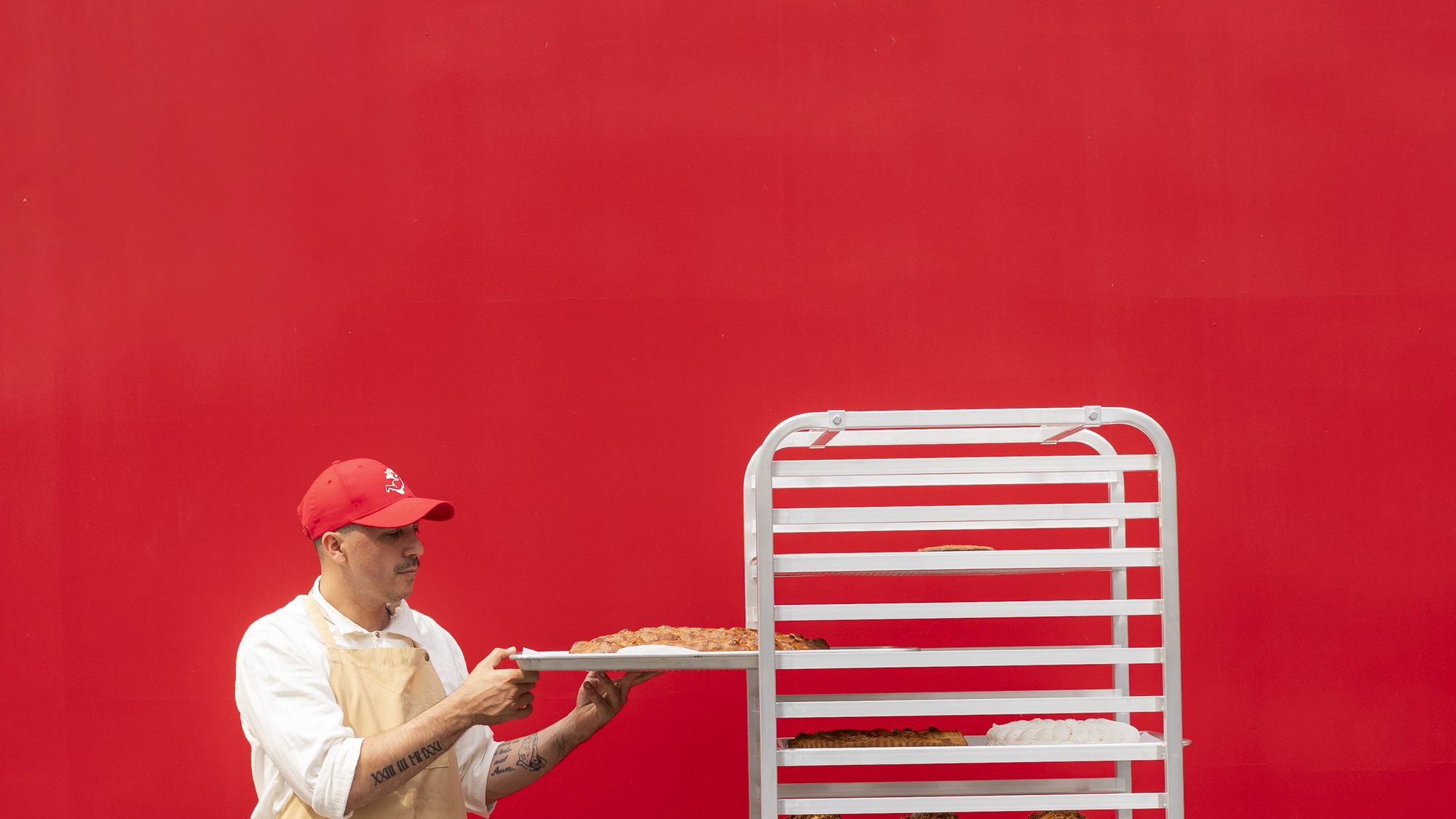 Panadero de Julia Bakery metiendo una bandeja al rack, contra la pared roja del local