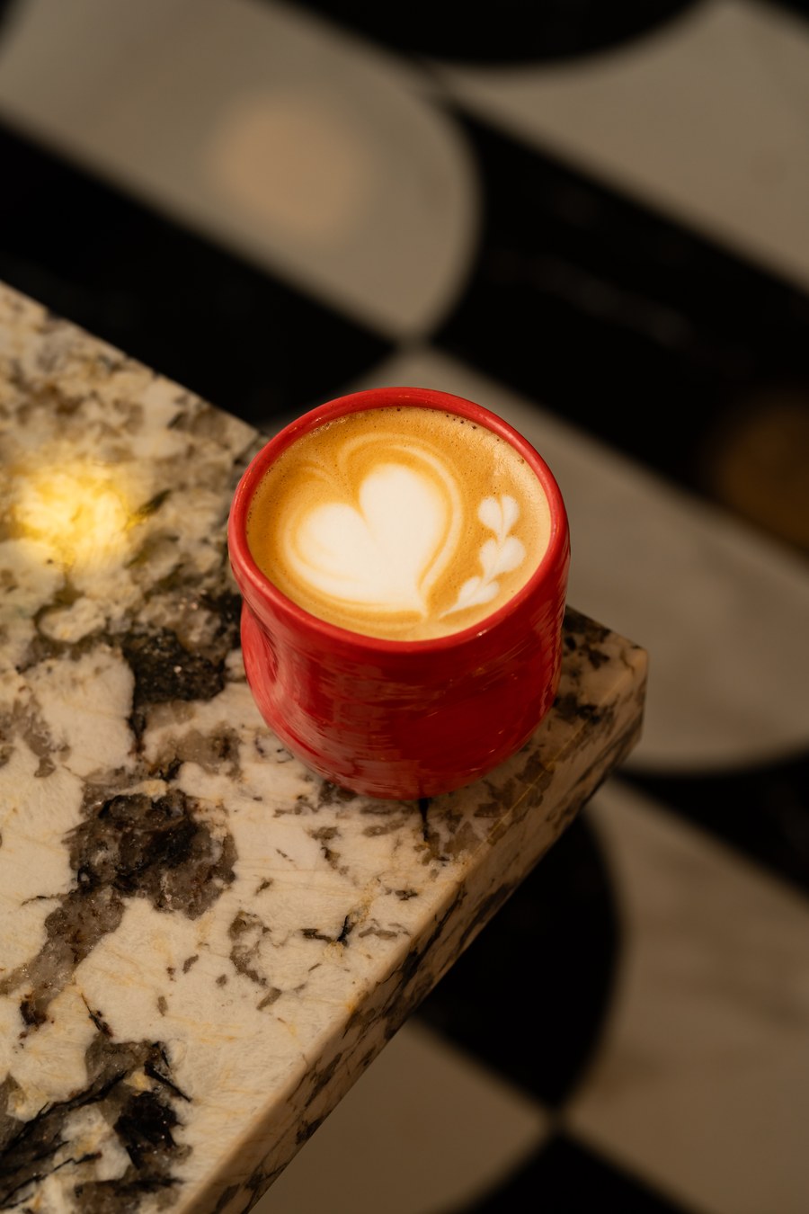 Latte con arte en taza roja sobre el mostrador de mármol