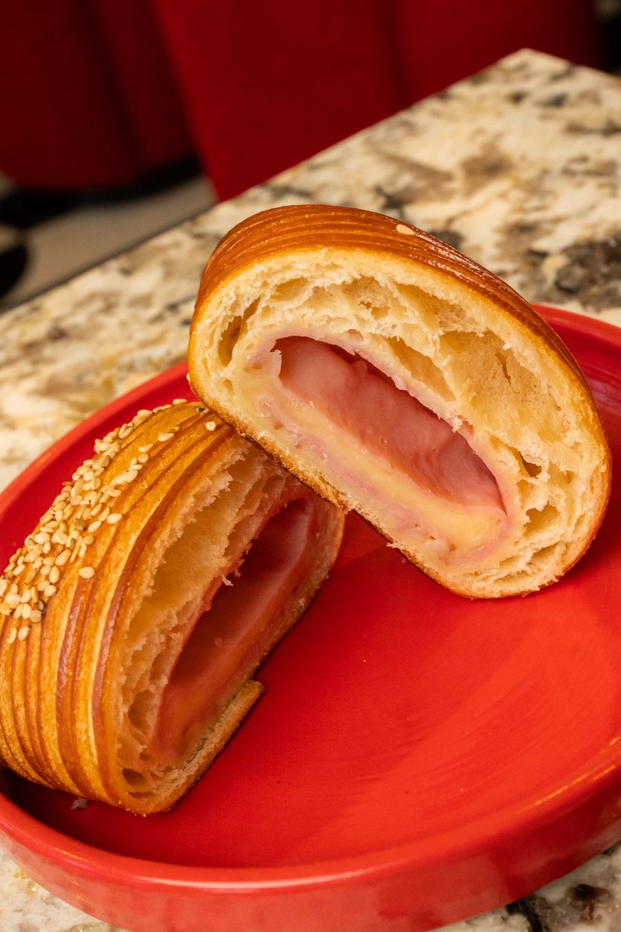 Croissant de jamón y queso partido, servido en plato rojo