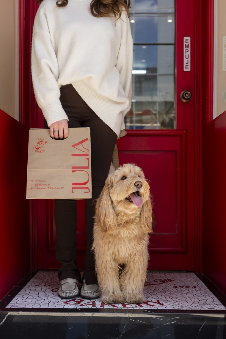 Perro esperando en la entrada de Julia Bakery junto a una bolsa de la panadería