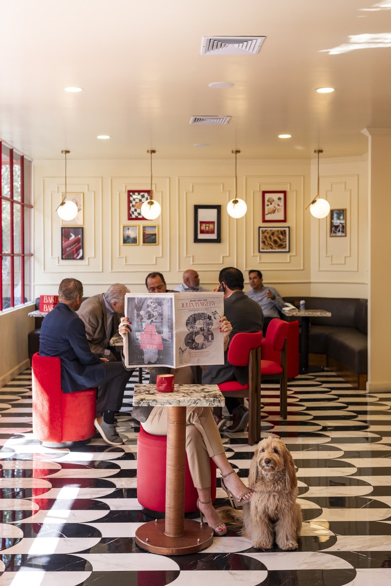 Salón de Julia Bakery con piso ajedrezado, sillas rojas y clientes en las mesas